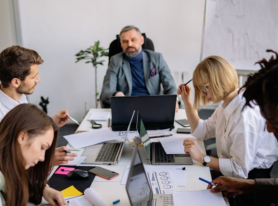 Grupo de personas reunido alrededor de una mesa con laptops, cuadernos y documentos