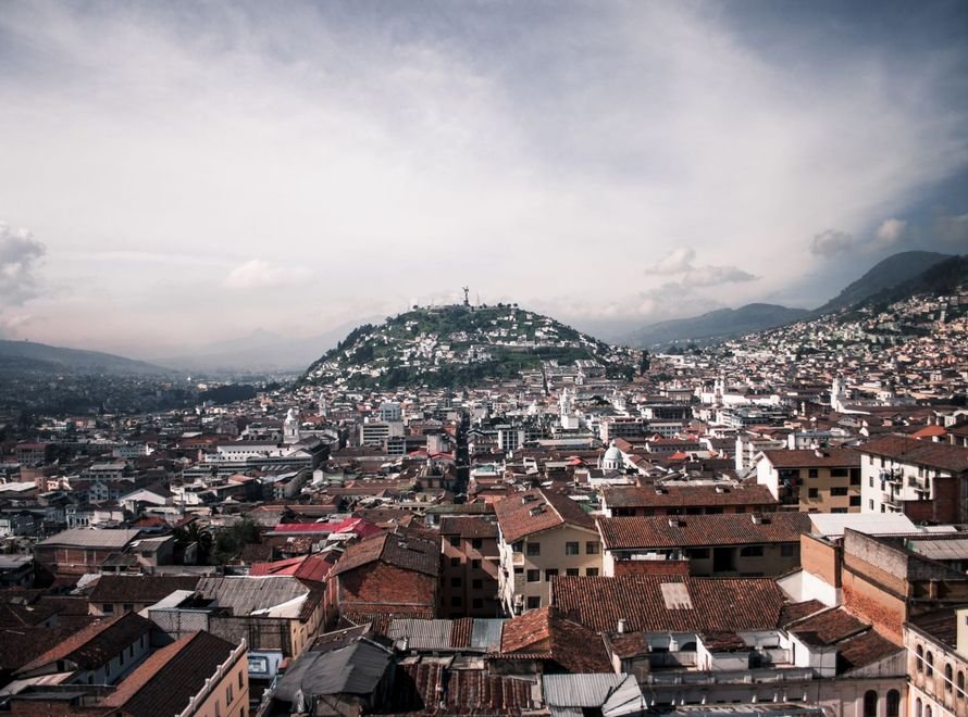 Vista panorámica de Quito con sus tejados y la loma del Panecillo bajo un cielo nublado