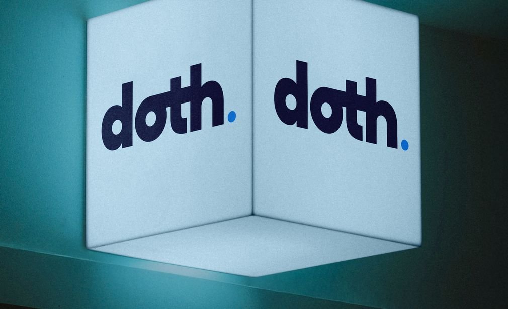 Cubo luminoso con el logo de DOTH sobre una pared iluminada en tonos azulados