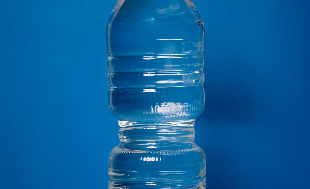 Botella transparente con agua sobre un fondo azul liso